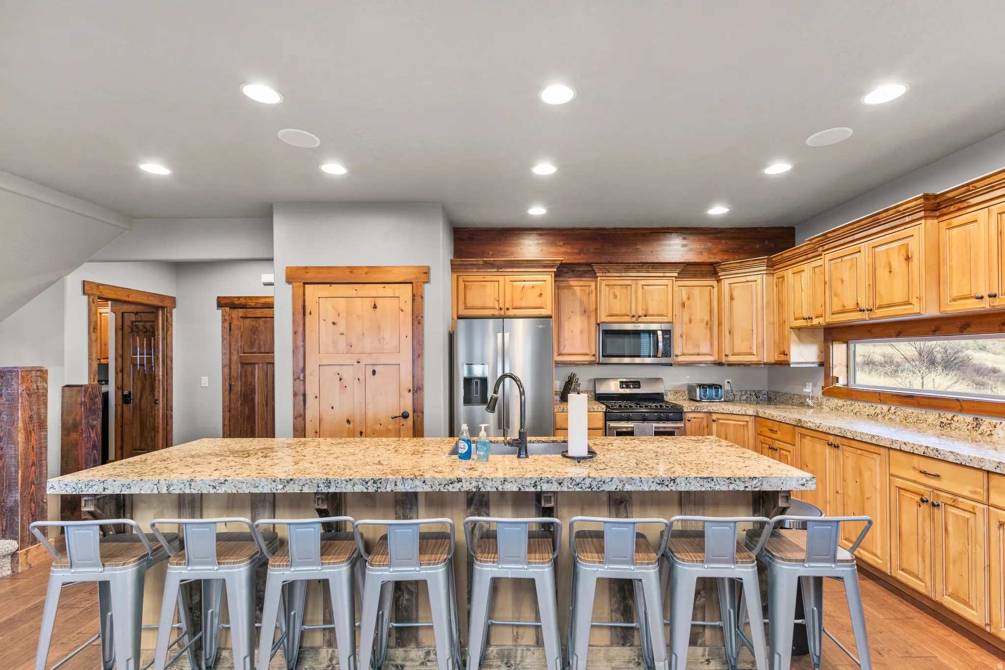 Kitchen featuring light wood-style flooring, a kitchen bar, appliances with stainless steel finishes, a spacious island, and light stone counters