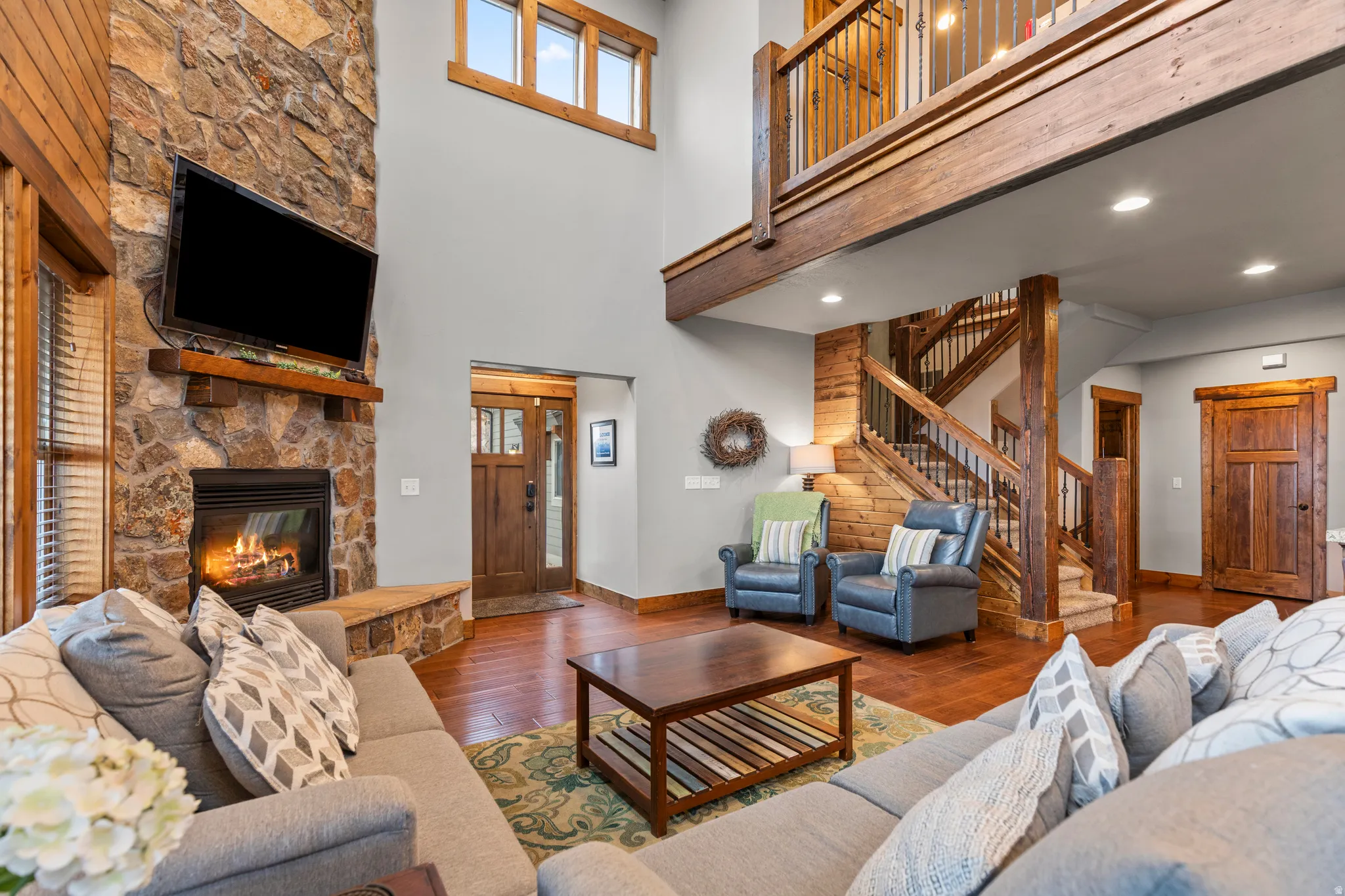 Living room with hardwood / wood-style floors, a high ceiling, stairway, a stone fireplace, and recessed lighting