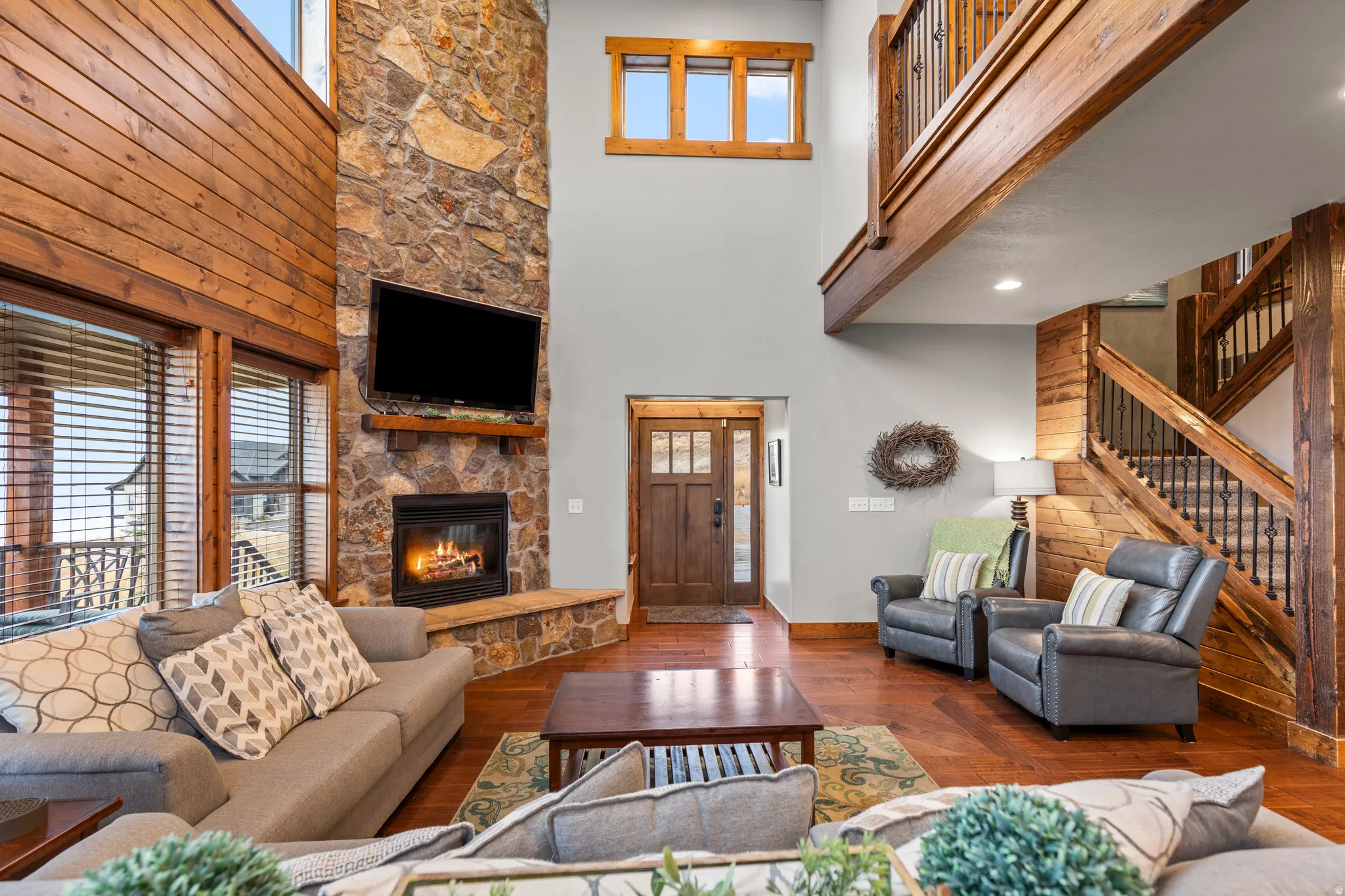 Living area featuring a towering ceiling, hardwood / wood-style floors, a stone fireplace, and stairs