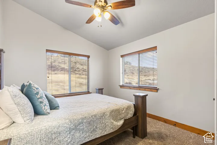 Carpeted bedroom featuring vaulted ceiling and a ceiling fan