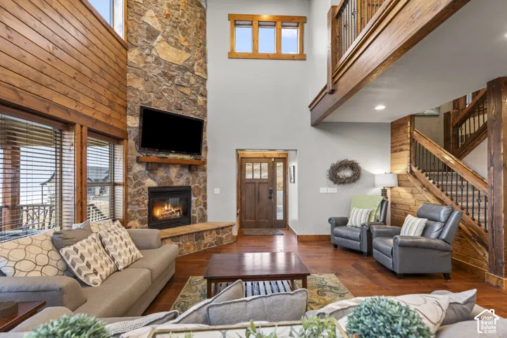 Living area featuring a towering ceiling, hardwood / wood-style floors, a stone fireplace, and stairs