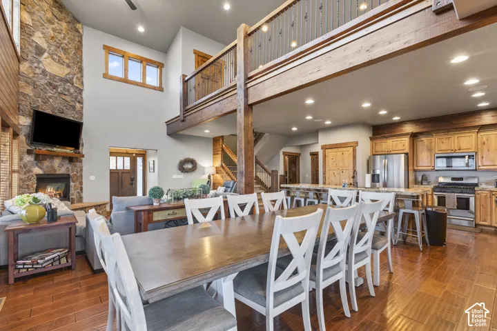 Dining room with a stone fireplace, stairway, dark wood-type flooring, recessed lighting, and a high ceiling