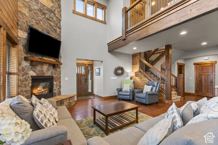 Living room with hardwood / wood-style floors, a high ceiling, stairway, a stone fireplace, and recessed lighting