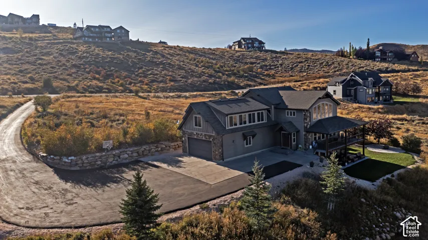 Exterior featuring a multilevel design, a covered deck, an attached two-car garage, and a sloped landscape with natural vegetation