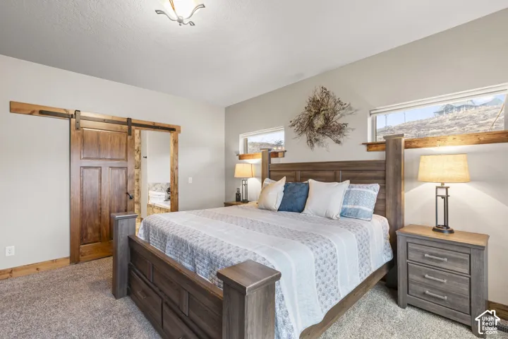 Bedroom with a barn door, ensuite bathroom, and light colored carpet