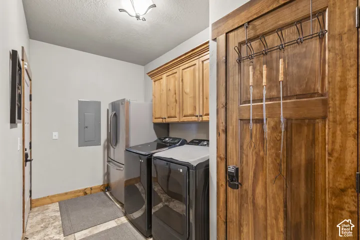 Washroom featuring cabinet space, electric panel, a textured ceiling, and washer and dryer