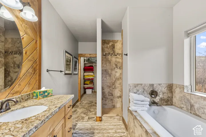Bathroom featuring vanity, a garden tub, a walk in closet, and tiled shower