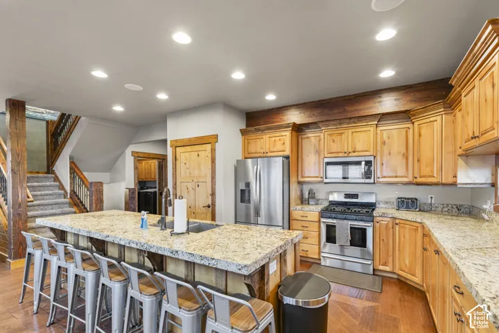 Kitchen featuring recessed lighting, appliances with stainless steel finishes, a breakfast bar area, an island with sink, and light stone counters