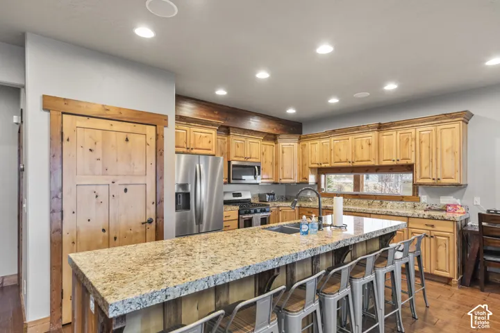 Kitchen featuring a kitchen breakfast bar, light wood finished floors, stainless steel appliances, recessed lighting, and an island with sink