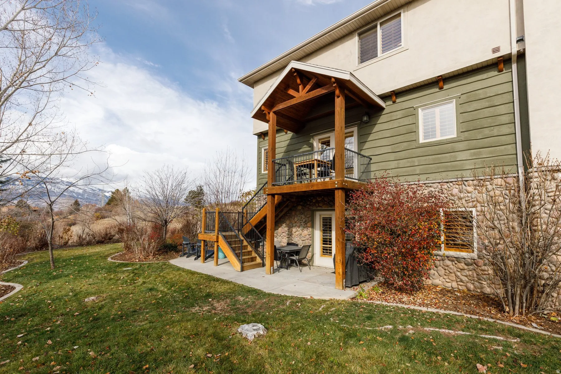 Back of property with a patio, stairs, a lawn, stone siding, and stucco siding