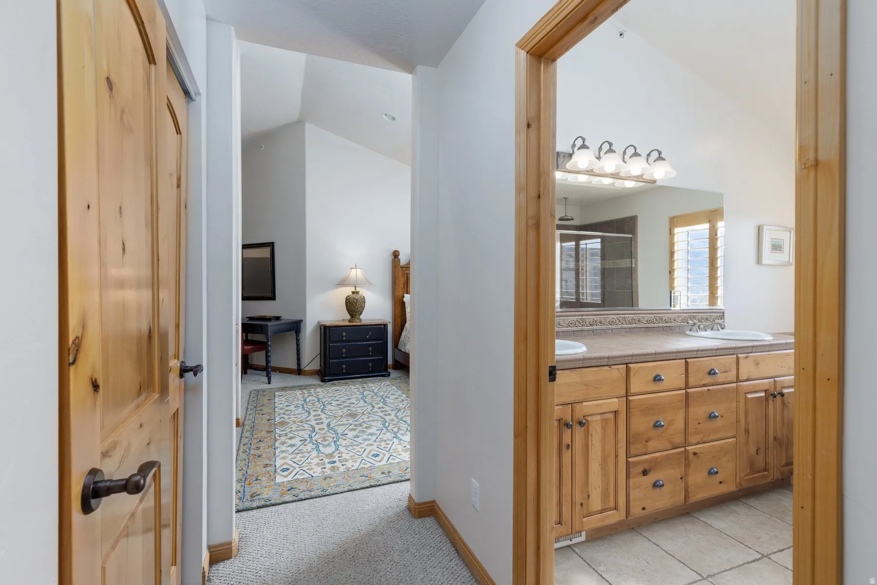 Bathroom with double vanity, light carpet, light tile patterned flooring, a shower stall, and vaulted ceiling
