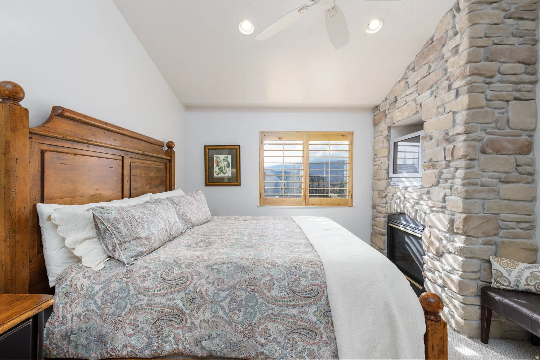 Bedroom with a stone fireplace, ceiling fan, and lofted ceiling