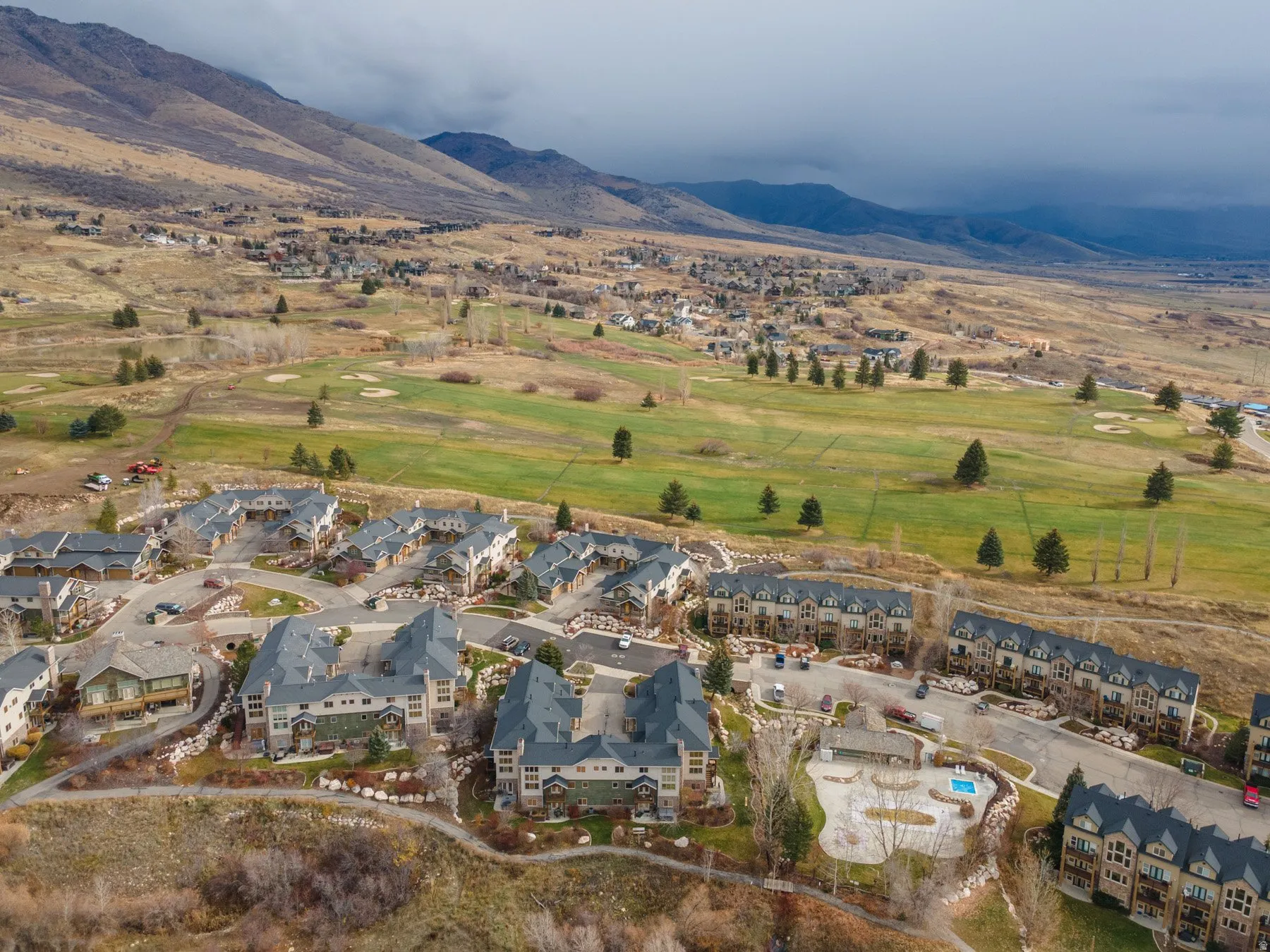 Aerial view of property and surrounding area featuring mountains, nearby suburban area, and a golf course