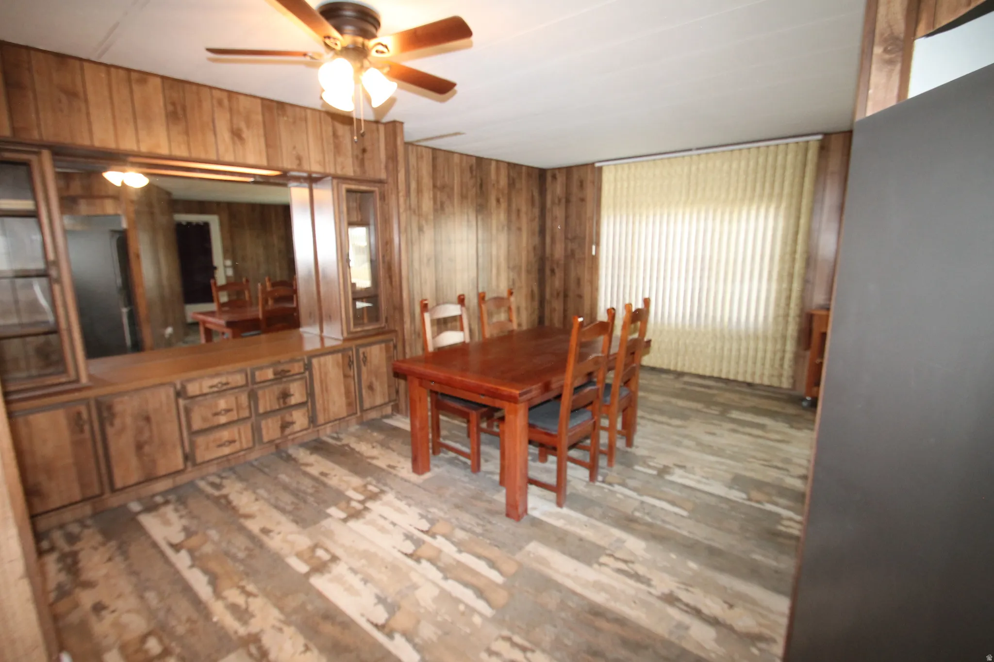 Dining area with light wood-style flooring, ceiling fan, and wood walls