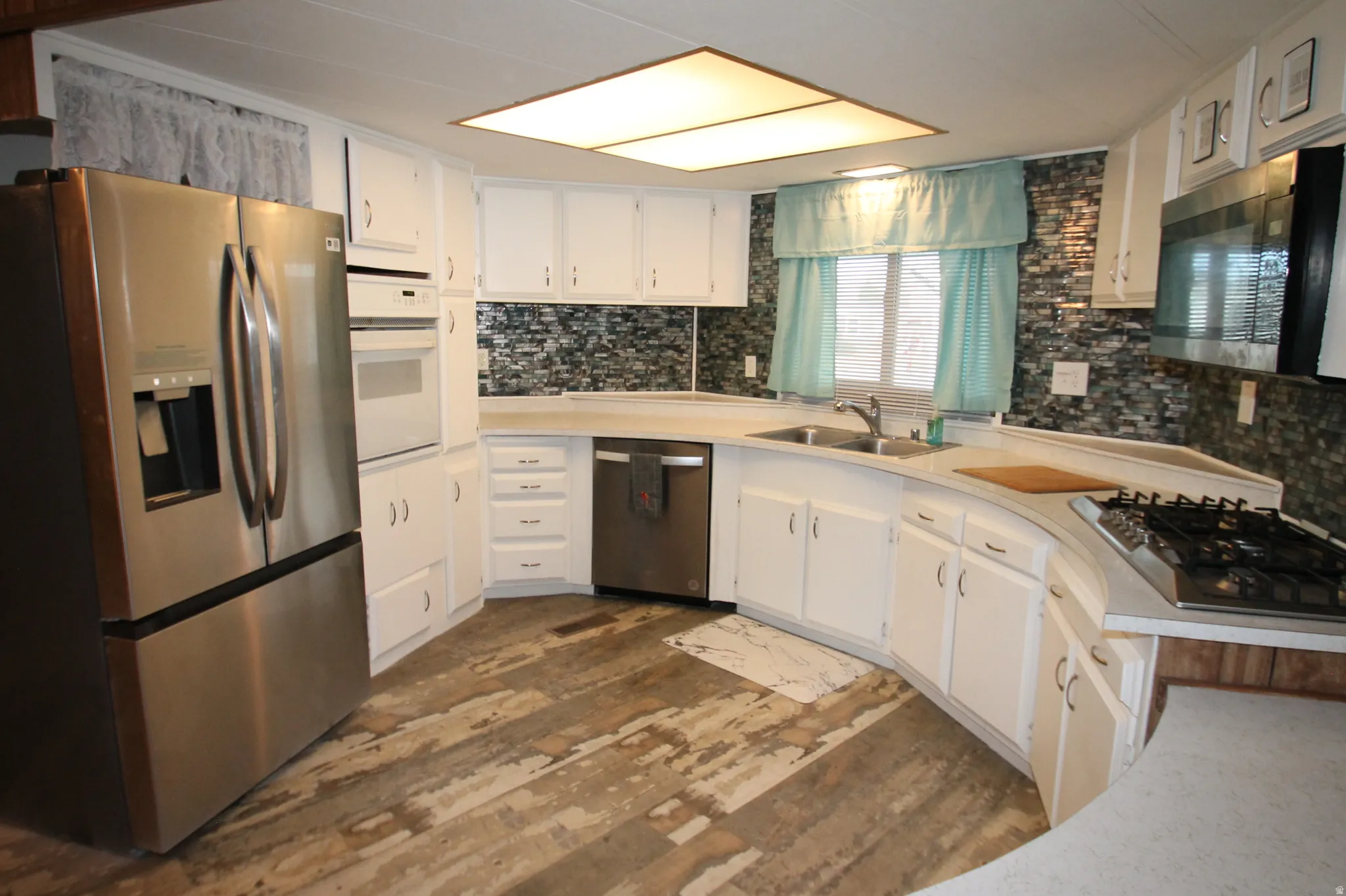 Kitchen featuring stainless steel appliances, light countertops, white cabinetry, dark wood-style flooring, and decorative backsplash