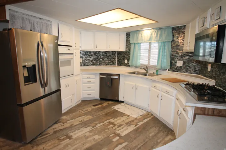 Kitchen featuring stainless steel appliances, light countertops, white cabinetry, dark wood-style flooring, and decorative backsplash