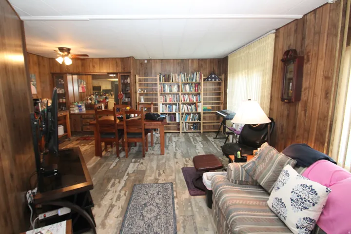 Living room with wood walls, light wood-type flooring, and ceiling fan