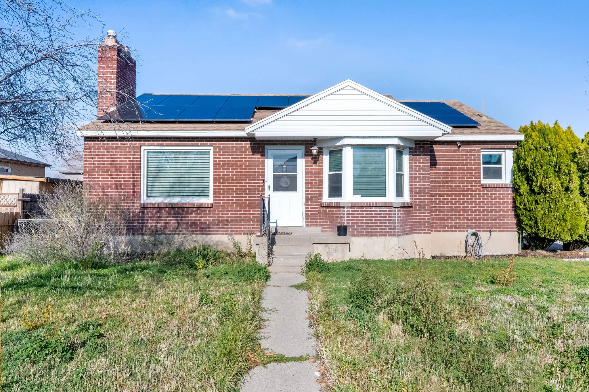 Bungalow featuring solar panels, brick siding, and a chimney