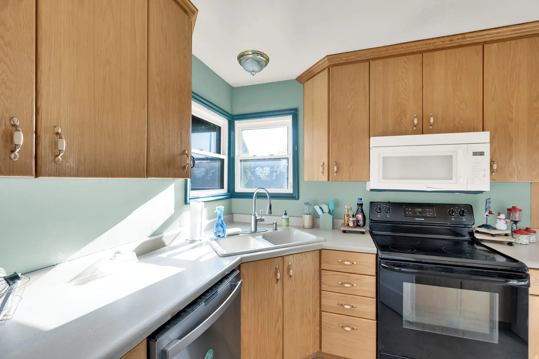 Kitchen featuring black range with electric cooktop, white microwave, light countertops, and dishwasher