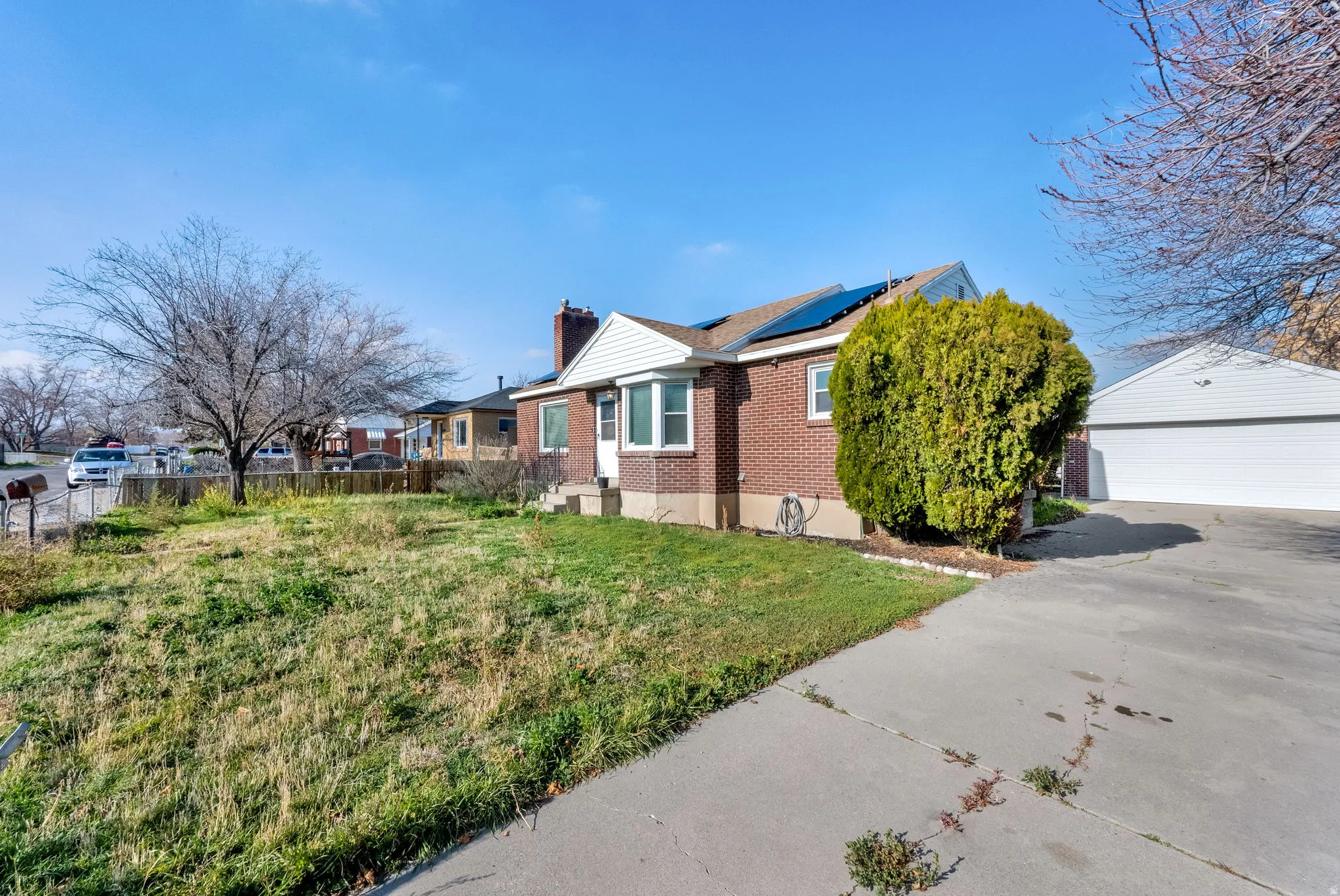 View of side of home with brick siding, roof mounted solar panels, a detached garage, a chimney, and an outdoor structure