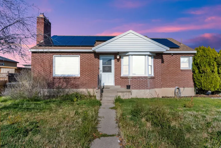 Bungalow with roof mounted solar panels, brick siding, and a chimney