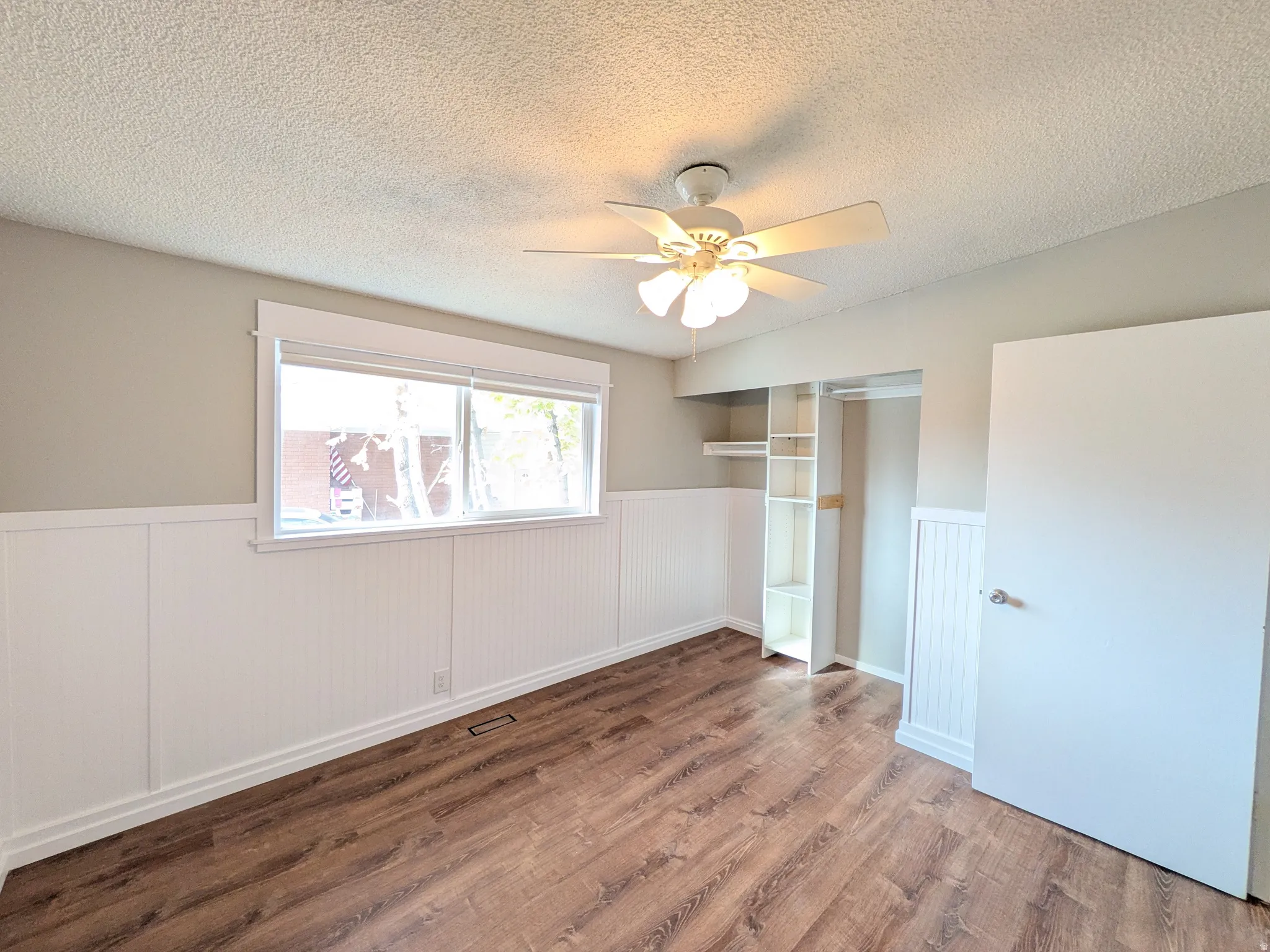 Unfurnished bedroom with a wainscoted wall, a closet, wood finished floors, ceiling fan, and a textured ceiling