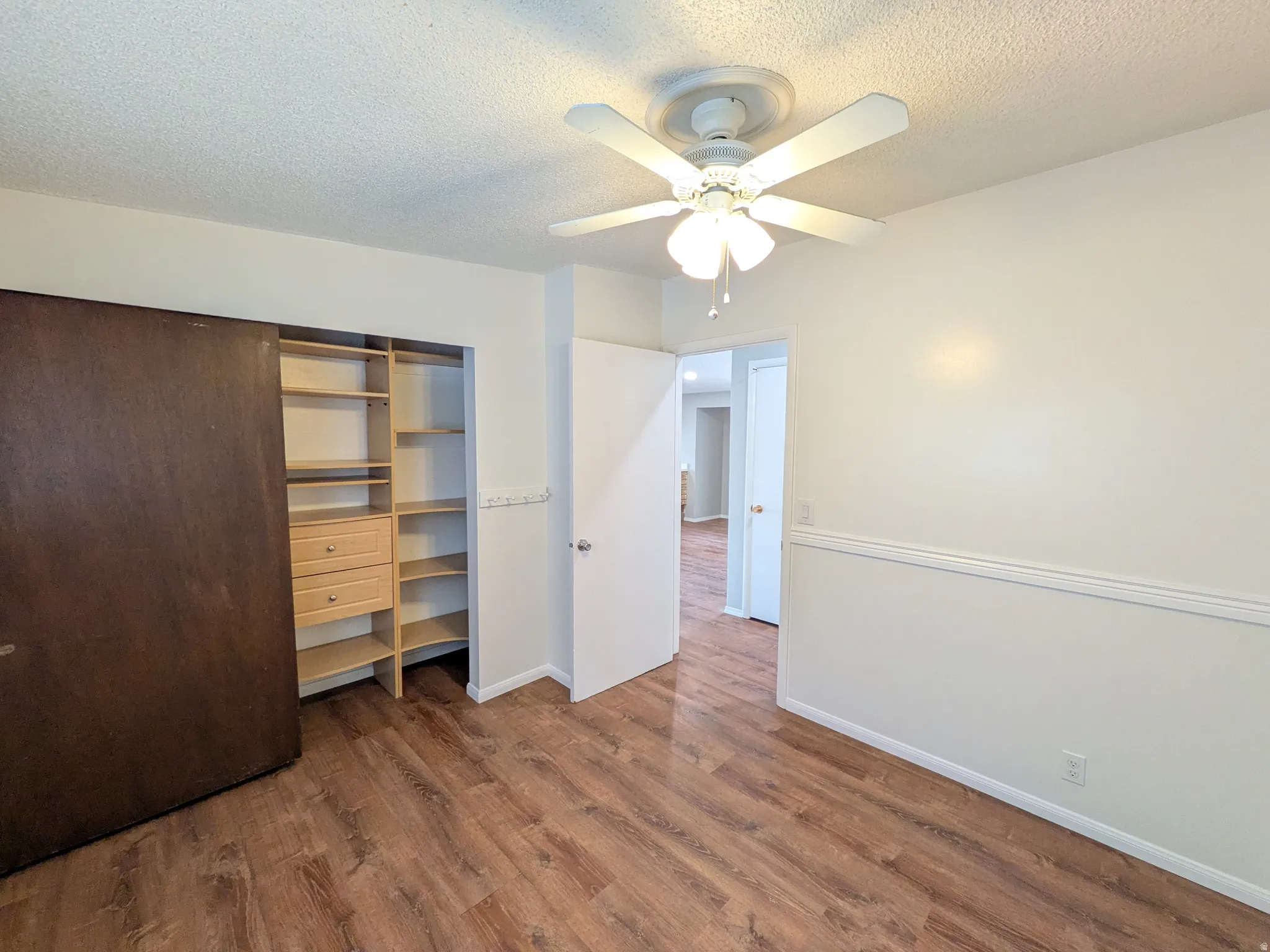 Bedroom with a textured ceiling, a ceiling fan, dark wood finished floors, and a closet