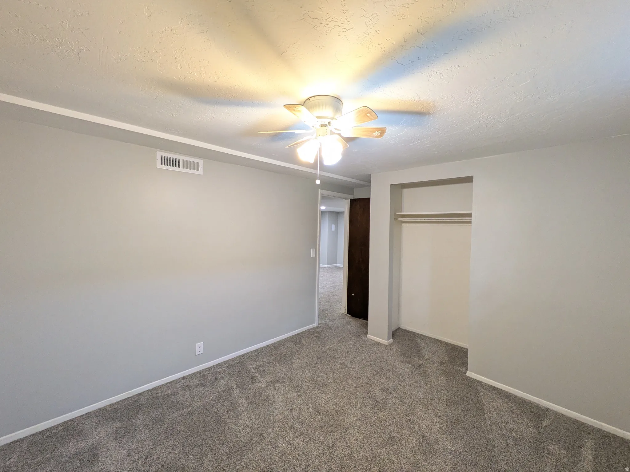 Unfurnished bedroom featuring a textured ceiling, carpet flooring, ceiling fan, and a closet