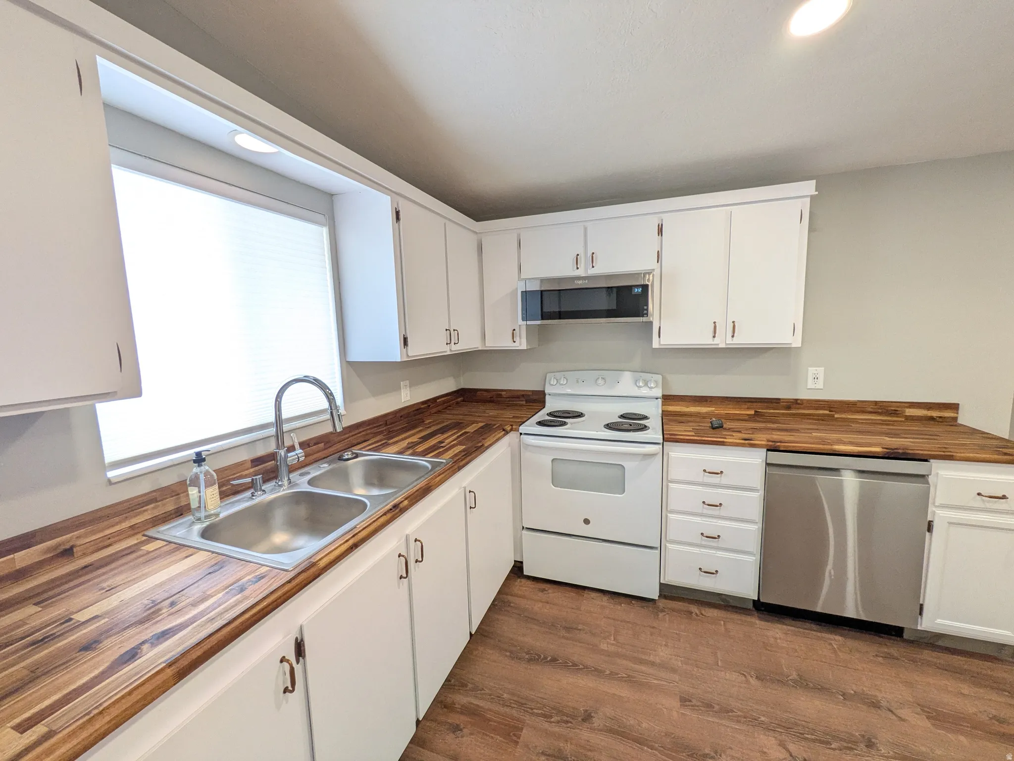 Kitchen featuring stainless steel appliances, butcher block countertops, white cabinets, dark wood-style flooring, and recessed lighting