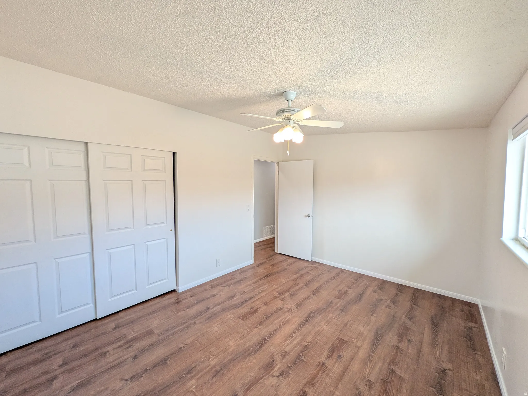 Unfurnished bedroom with a textured ceiling, a closet, wood finished floors, and a ceiling fan