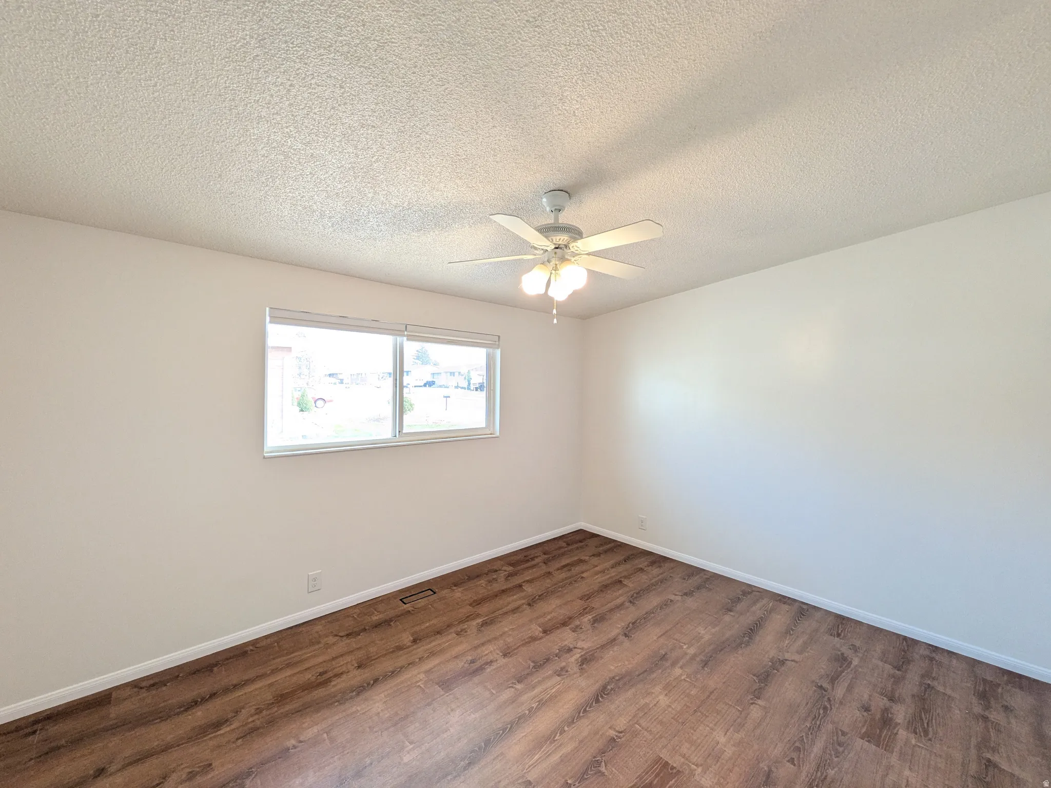 Empty room with dark wood-type flooring, a textured ceiling, and a ceiling fan