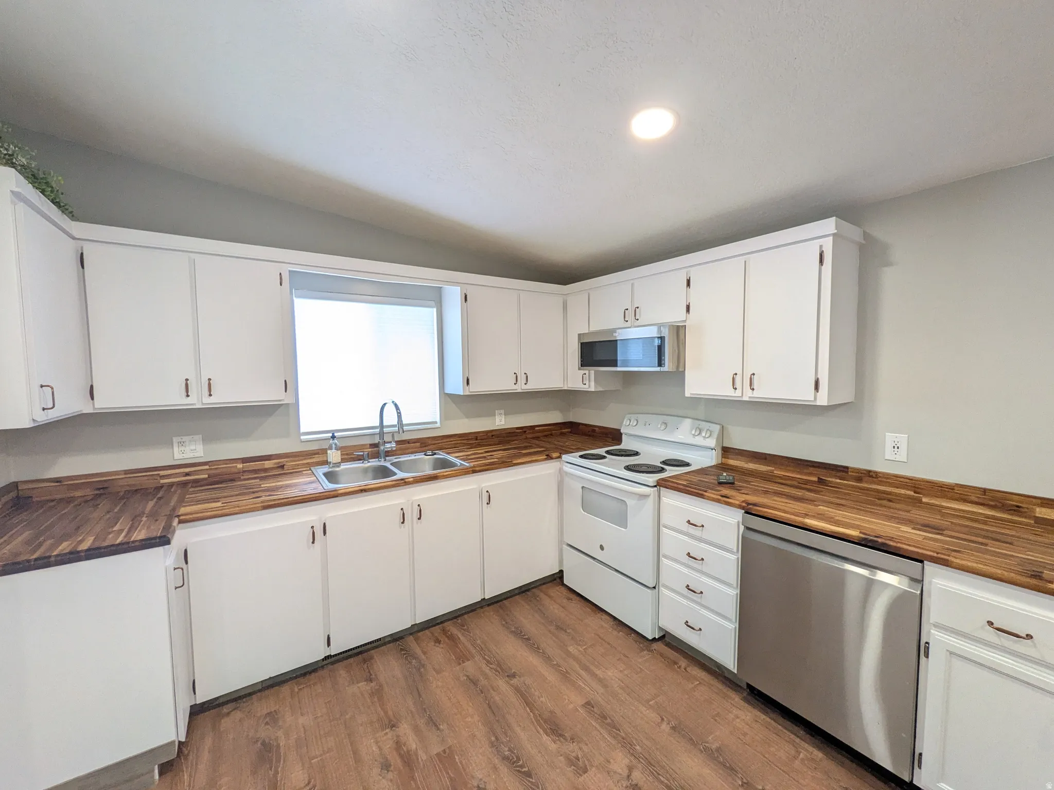 Kitchen with stainless steel appliances, white cabinets, wood counters, and dark wood-style floors