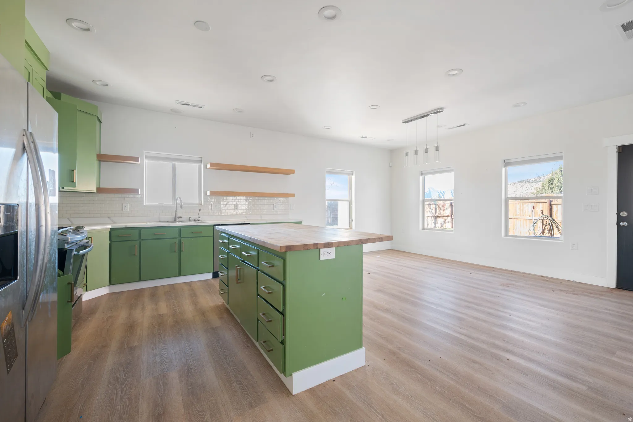 Kitchen with green cabinetry, open shelves, a center island, stainless steel appliances, and hanging light fixtures