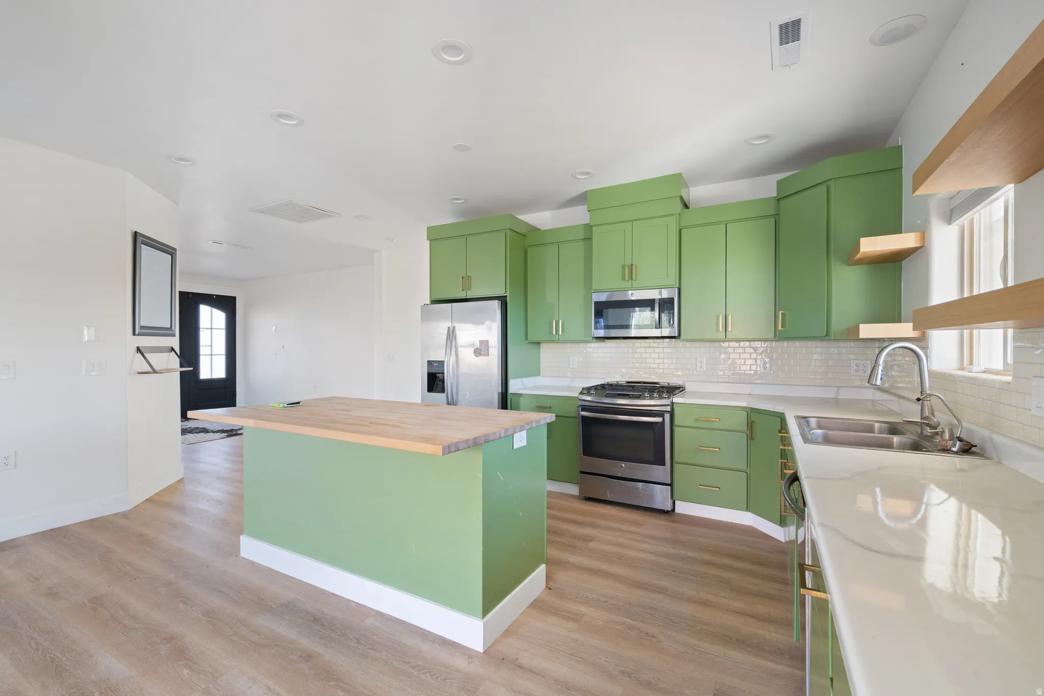 Kitchen featuring open shelves, green cabinetry, wood counters, stainless steel appliances, and a kitchen island
