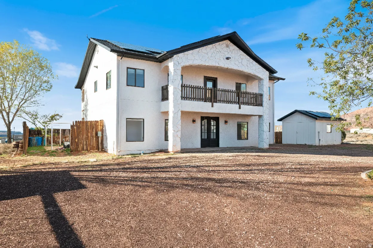 Rear view of house featuring a balcony, french doors, an outbuilding, stucco siding, and roof mounted solar panels