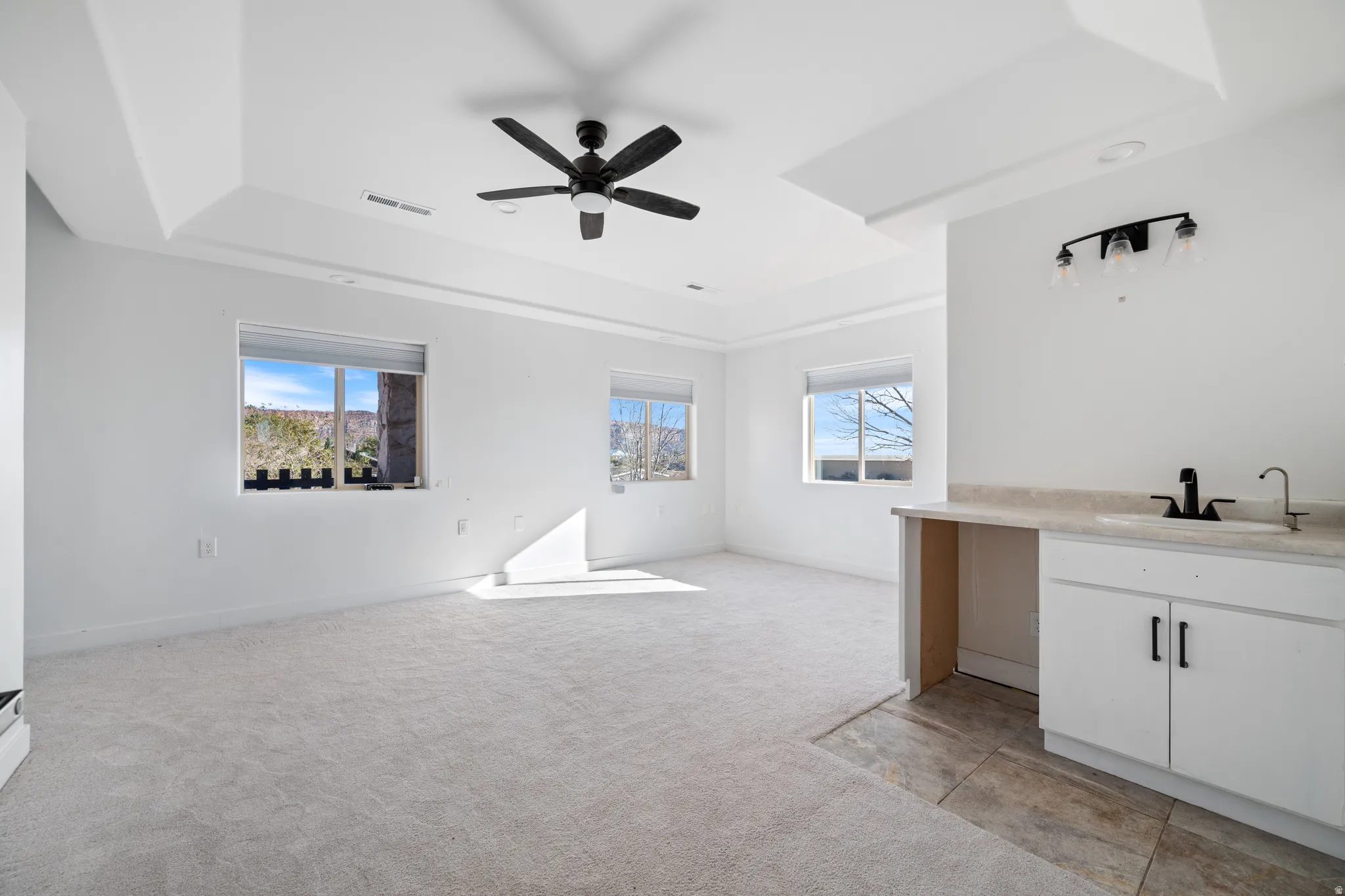 Unfurnished living room featuring light colored carpet, a raised ceiling, plenty of natural light, and a ceiling fan