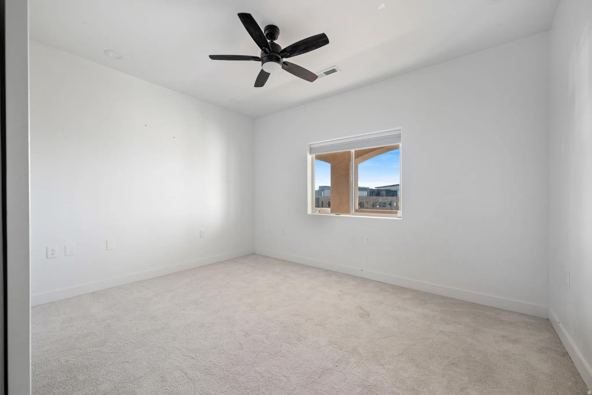 Empty room with light colored carpet and a ceiling fan