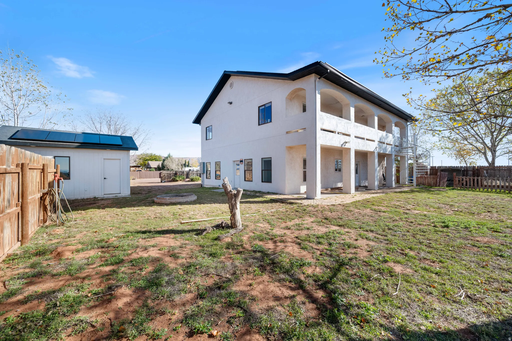 Rear view of property featuring a fenced backyard, a patio area, a balcony, a storage shed, and stucco siding