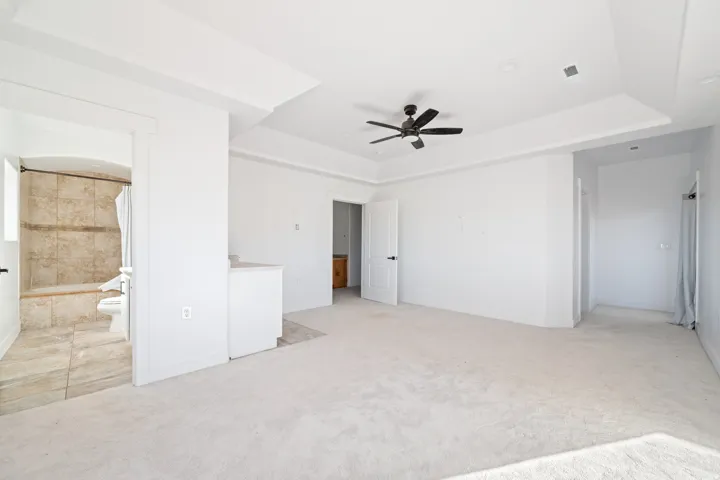 Unfurnished bedroom featuring light colored carpet, ceiling fan, ensuite bath, and a tray ceiling