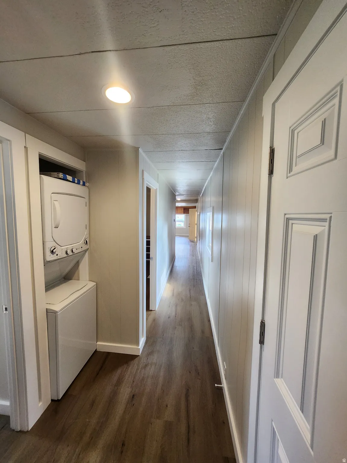Hallway featuring estacked washer and dryer, dark wood finished floors, wooden walls, and crown molding