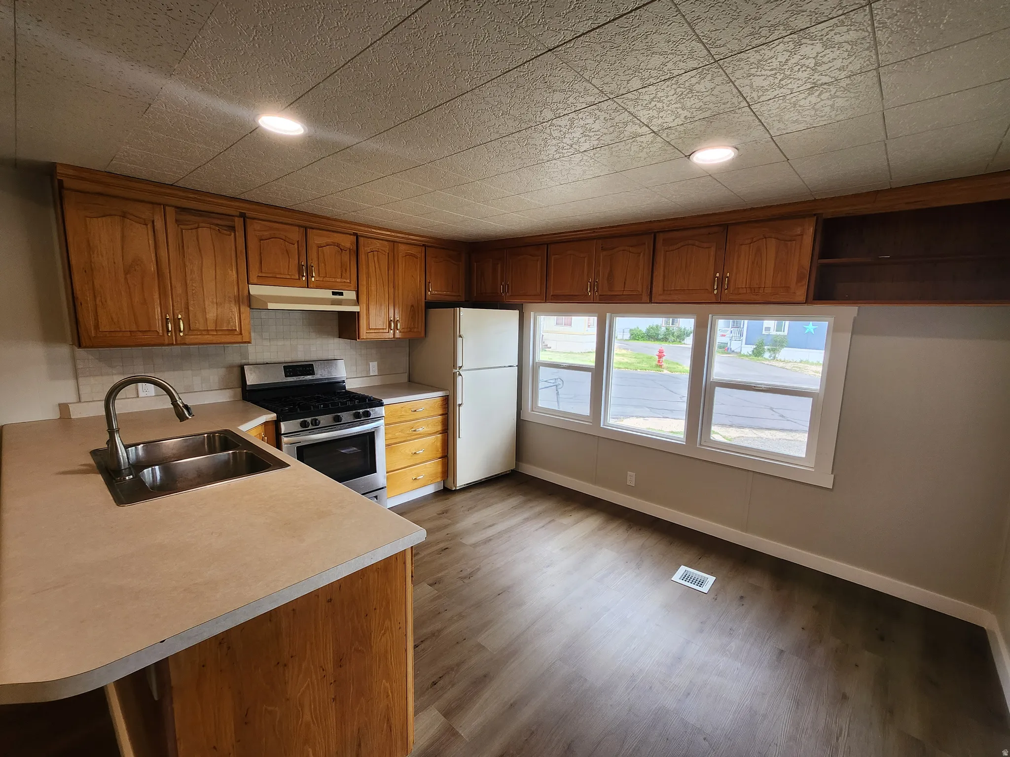 Kitchen featuring brown cabinets, stainless steel gas range oven, freestanding refrigerator, light countertops, and dark wood-type flooring