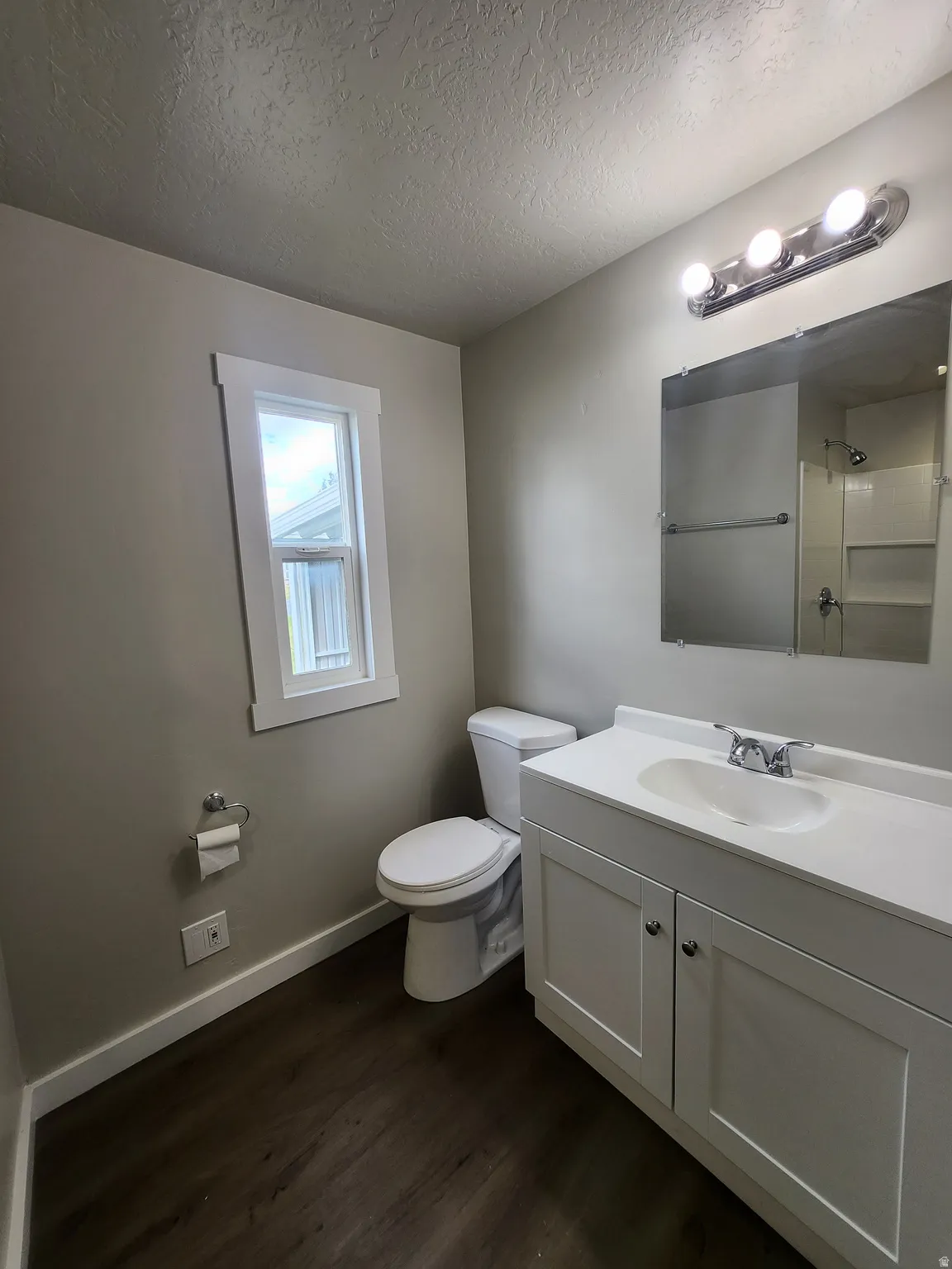 Full bath with vanity, a textured ceiling, dark wood finished floors, and a shower