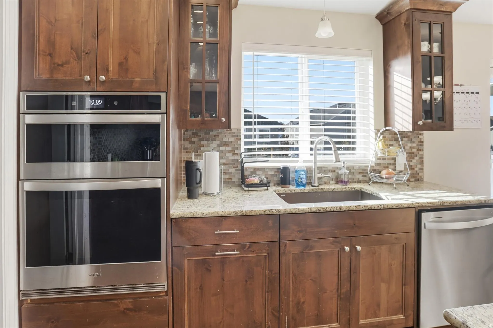 Kitchen featuring glass insert cabinets, stainless steel appliances, light stone counters, and backsplash