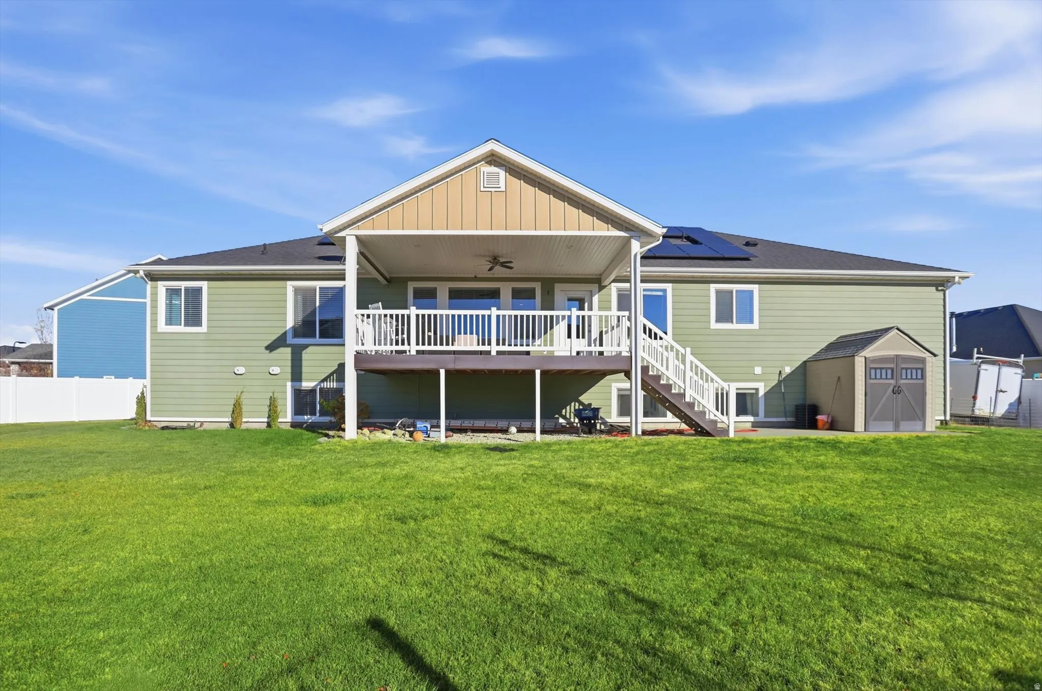 Rear view of property featuring ceiling fan, a shed, stairs, a wooden deck, and solar panels