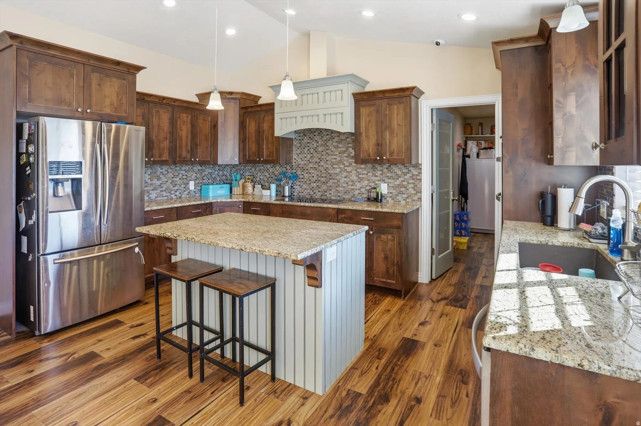 Kitchen featuring hanging light fixtures, stainless steel refrigerator with ice dispenser, lofted ceiling, backsplash, and light stone counters
