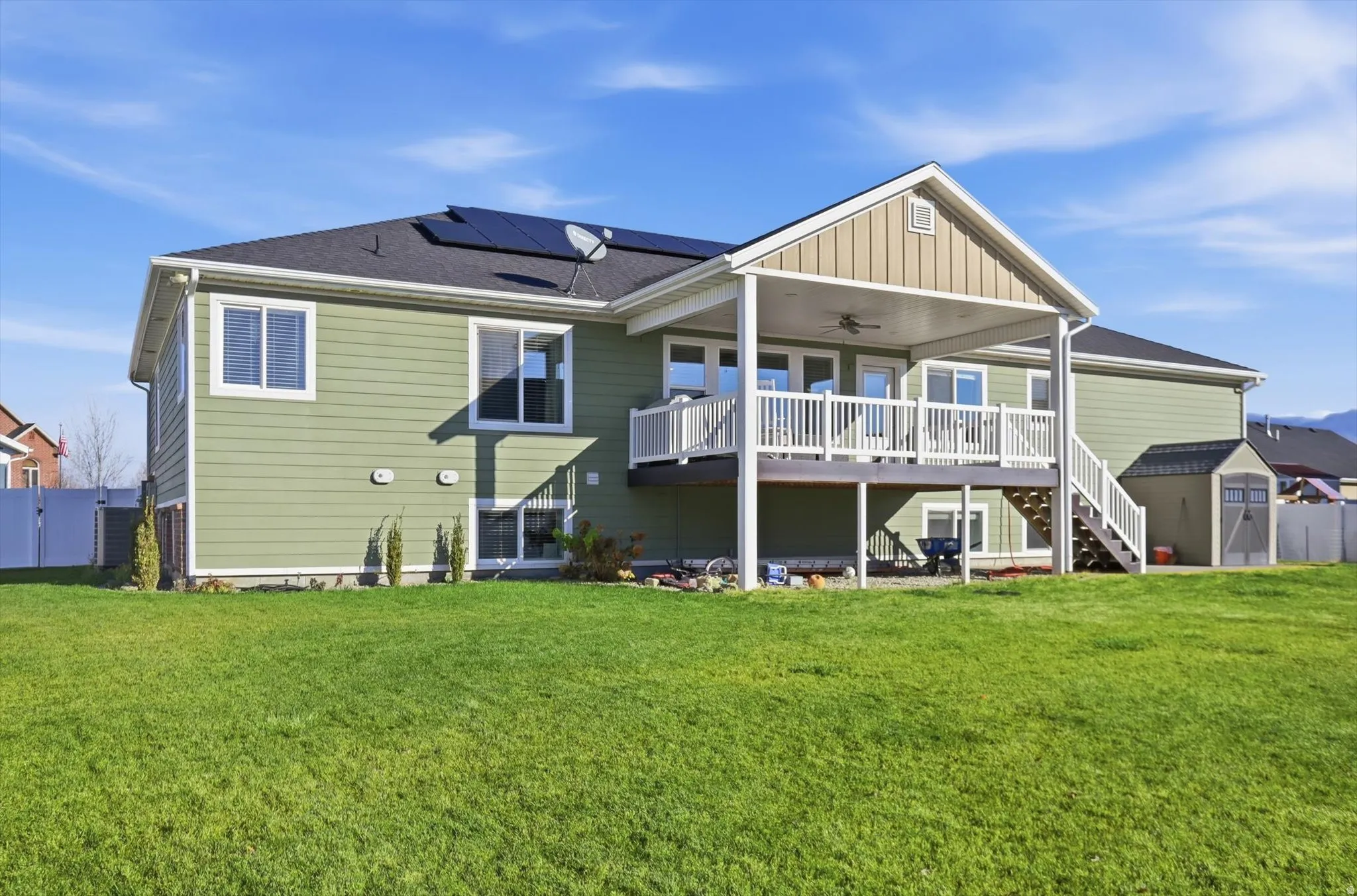 Rear view of property with stairs, a ceiling fan, a wooden deck, a storage shed, and roof mounted solar panels
