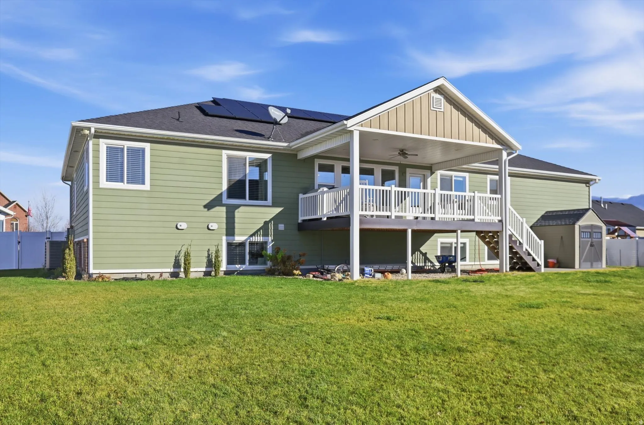 Rear view of property featuring ceiling fan, stairway, a wooden deck, a storage shed, and roof mounted solar panels