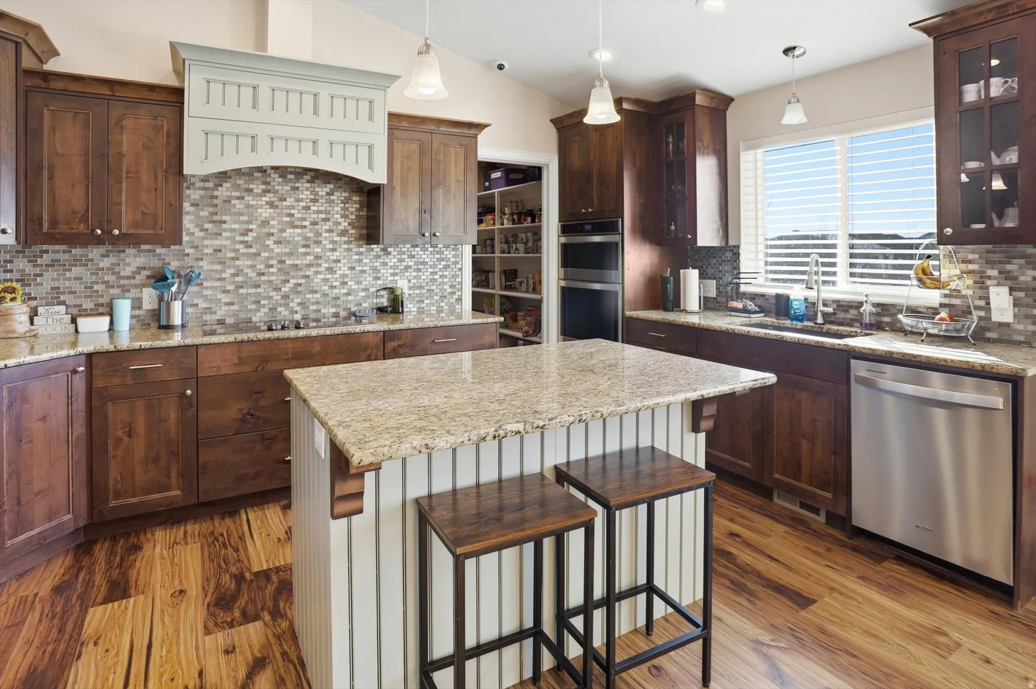 Kitchen with backsplash, hanging light fixtures, appliances with stainless steel finishes, a breakfast bar, and lofted ceiling