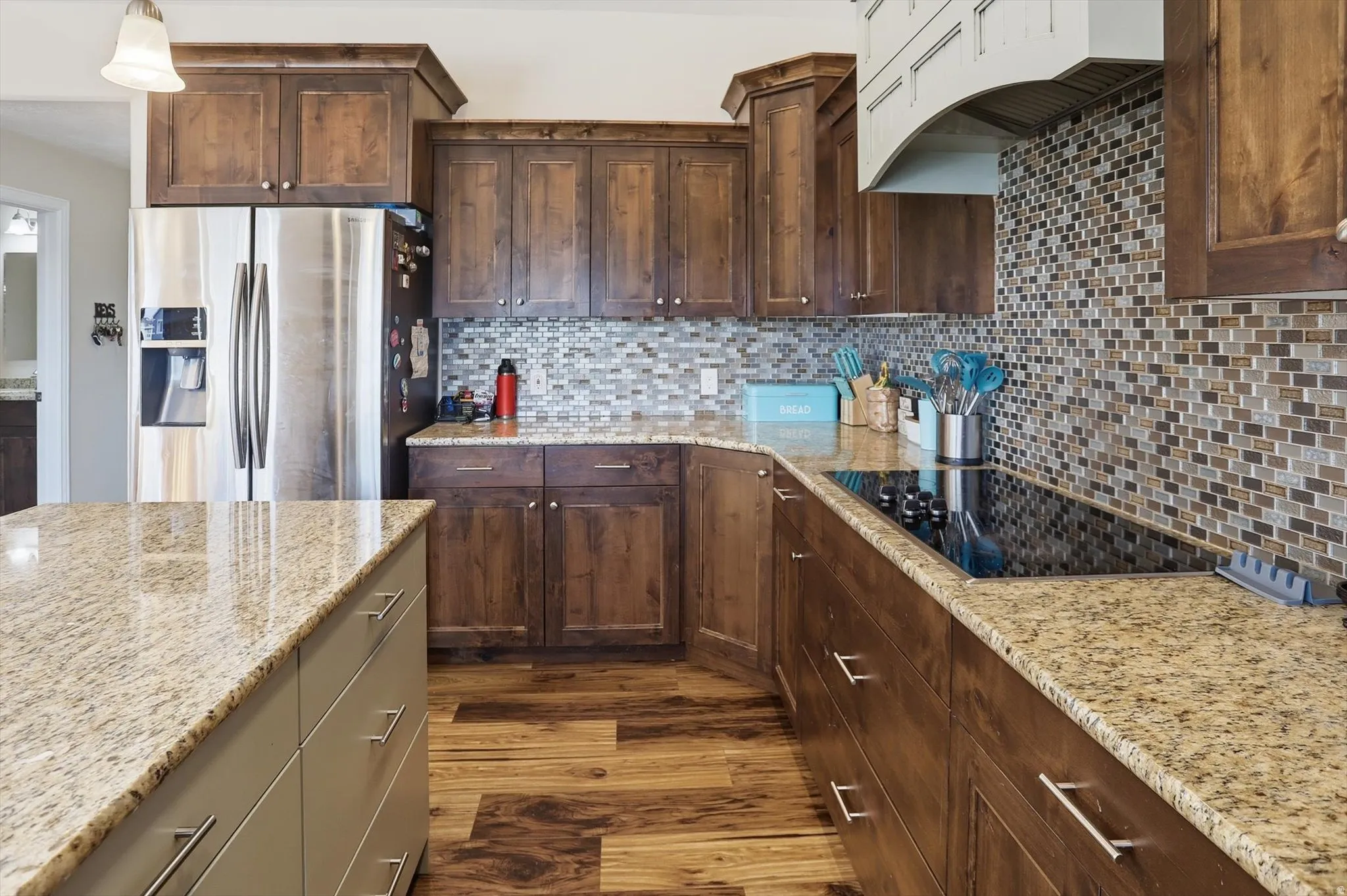 Kitchen with stainless steel fridge, under cabinet range hood, dark wood-type flooring, black electric stovetop, and decorative backsplash