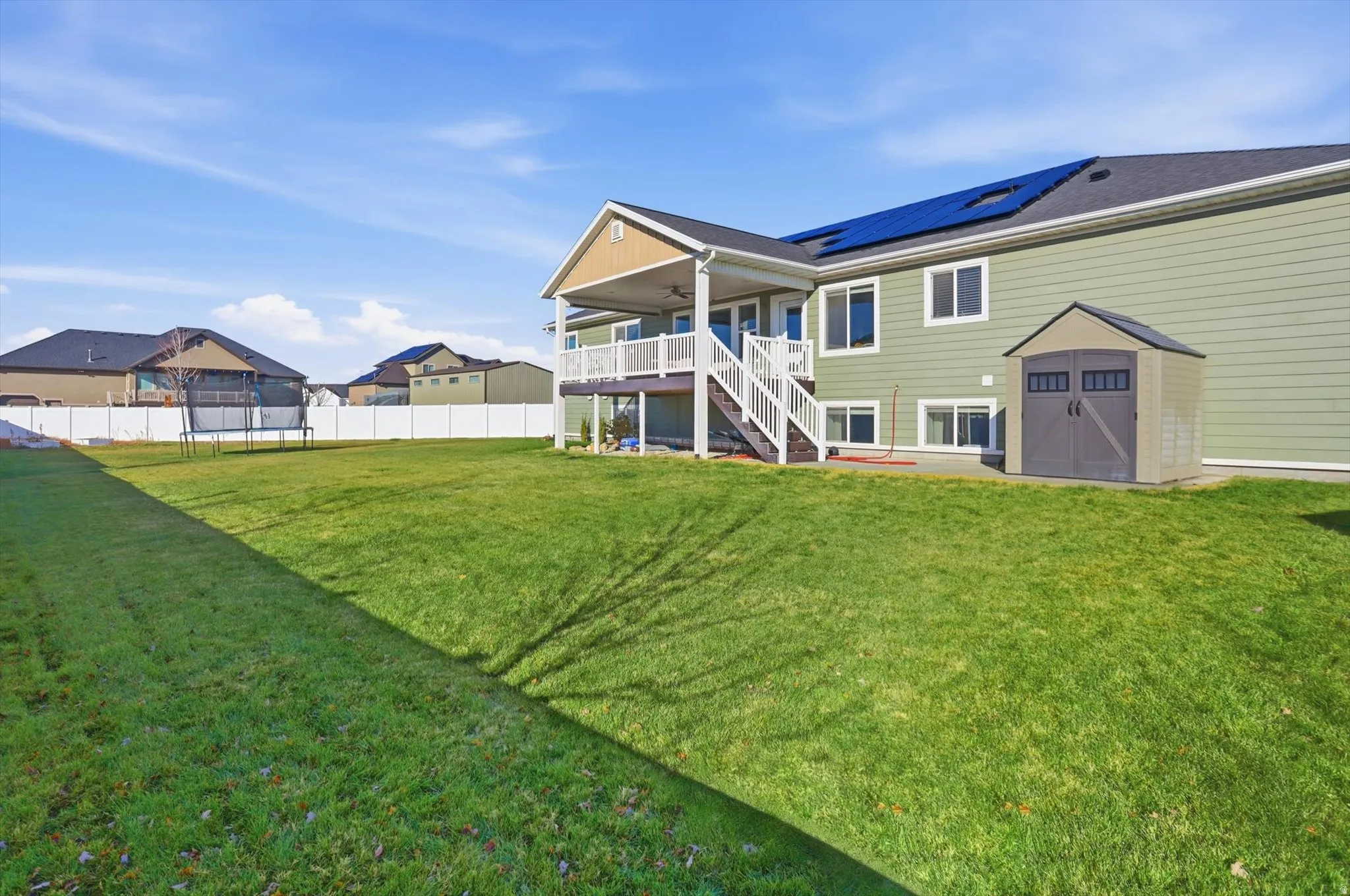 Back of property featuring a trampoline, stairs, a storage unit, a patio area, and roof mounted solar panels